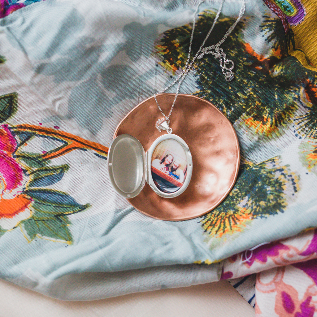 silver evelyn locket with picture of two best friends inside on a rose gold plate with a colored scarf underneath