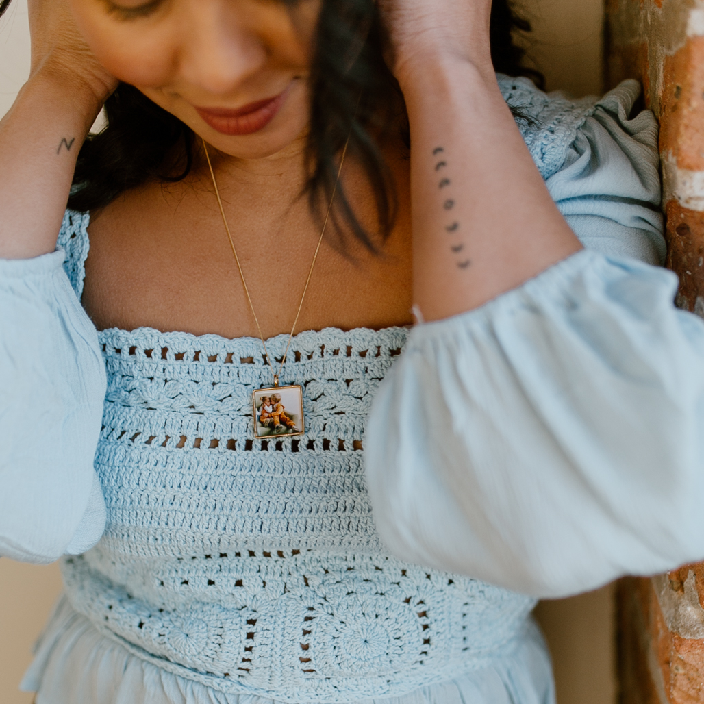 woman with black hair and blue blouse with gold locket photograph inside