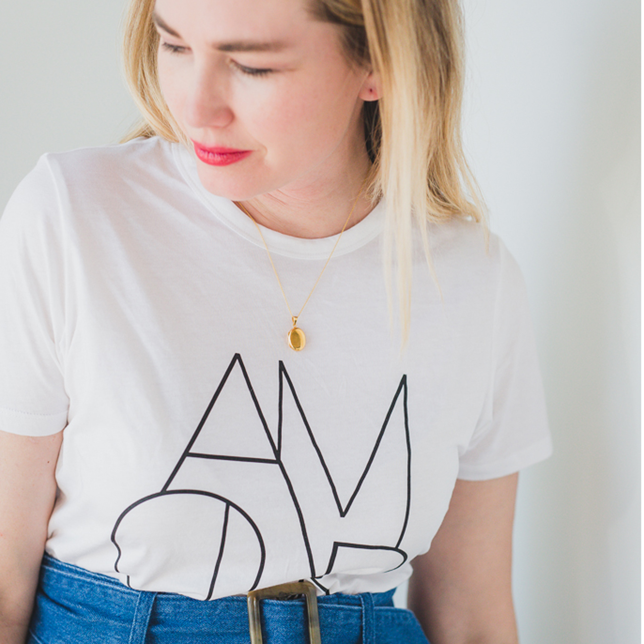 little gold oval locket that holds photos inside worn by a woman with a white shirt and denim skirt.