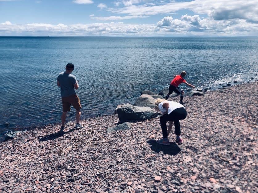 three people throwing rocks in lake superior at brighton beach