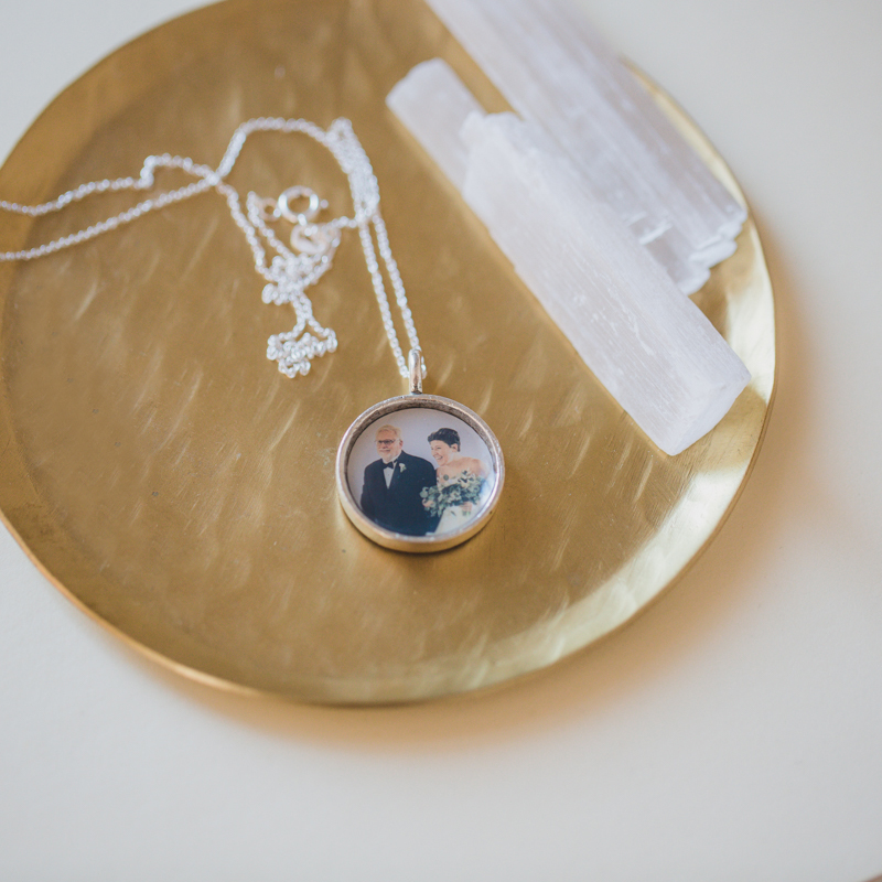 an open faced silver locket pendant with a photo of a female-presenting bride walking down the isle on her wedding day with a male father figure