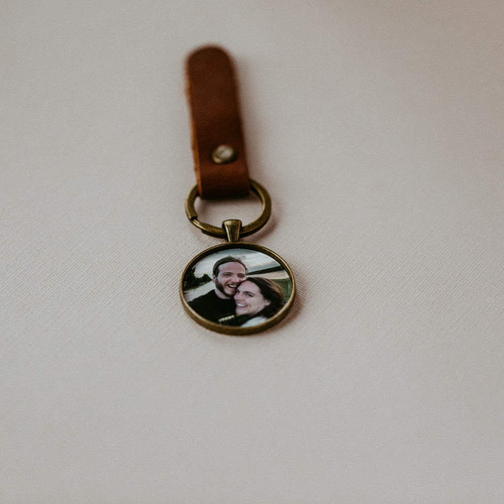 bronze picture pendant locket with photo of couple inside attached to leather keychain on white backdrop