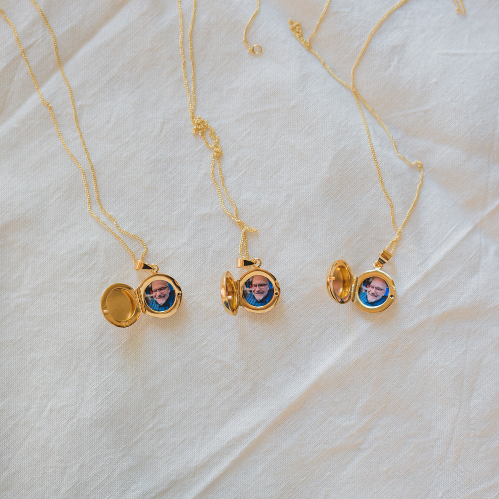 three small gold round little circle lockets with a photograph of their dad smiling inside on a white linen